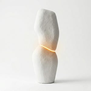 Puede incluir: Una escultura abstracta blanca con una superficie texturizada. La escultura est&aacute; dividida por una banda horizontal de luz c&aacute;lida y brillante. La forma es org&aacute;nica y se asemeja a dos formas redondeadas apiladas.