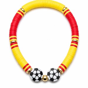 May include: A vibrant necklace featuring alternating sections of yellow and red disc beads. The necklace includes two soccer ball-shaped charms and gold-colored accents. The necklace is designed to be worn around the neck.