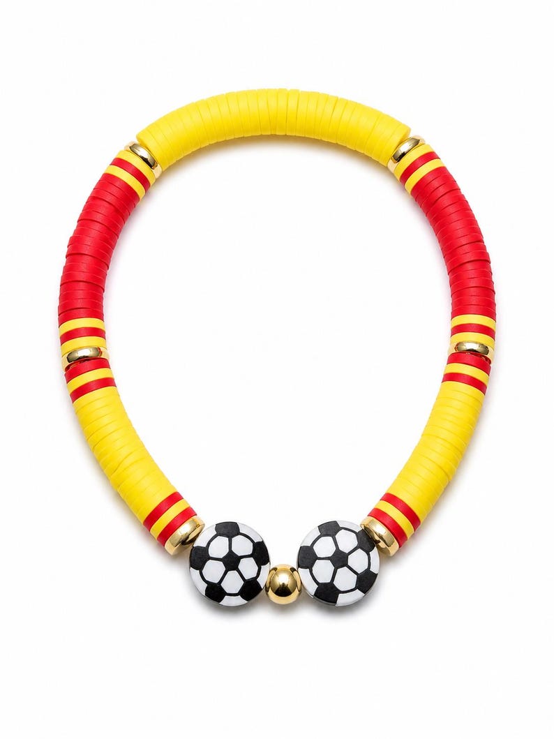 May include: A vibrant necklace featuring alternating sections of yellow and red disc beads. The necklace includes two soccer ball-shaped charms and gold-colored accents. The necklace is designed to be worn around the neck.
