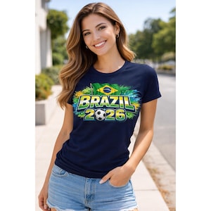 May include: A navy blue t-shirt featuring the text "BRAZIL 2026" in green and yellow, a football, and the Brazilian flag. The t-shirt is short-sleeved with a crew neck.