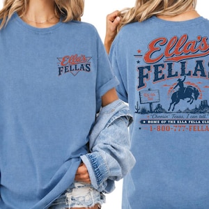 A woman wearing a blue t-shirt with the text "Ellas Fellas" printed on it, along with a graphic of a cowboy on a horse.