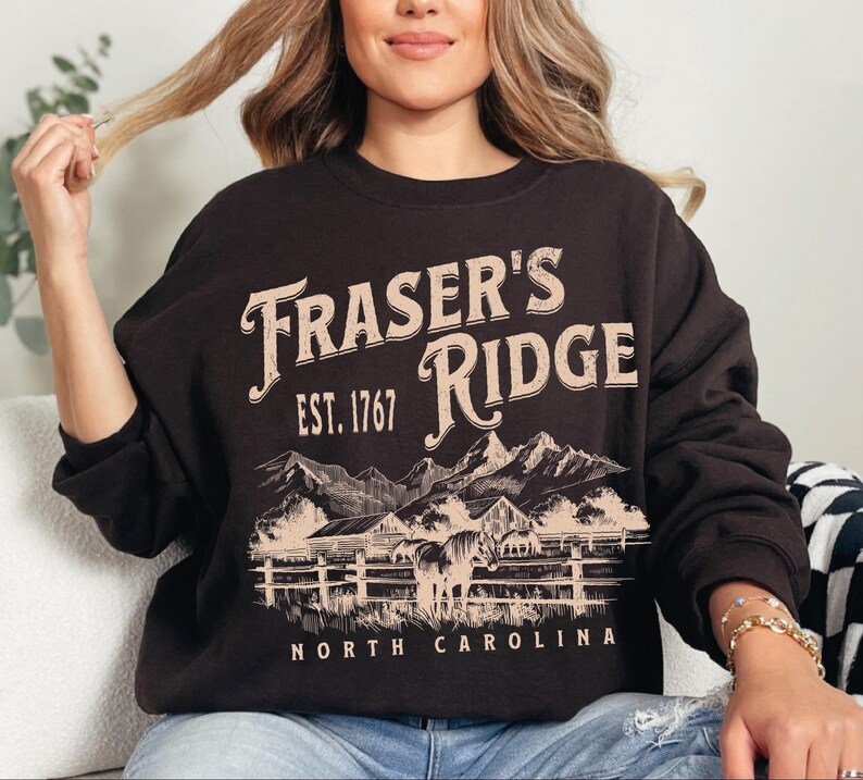 A woman wearing a black sweatshirt with a graphic design of a mountain range and the text "Fraser's Ridge" printed on it.