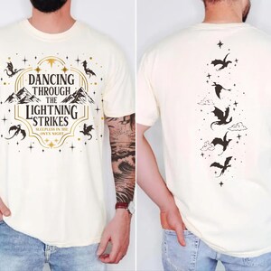 A white t-shirt with a graphic design featuring a dragon and the text "DANCING THROUGH THE LIGHTNING STRIKES ONY NIGHT" printed on it.