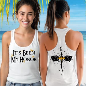 A smiling woman wearing a white tank top with text and a graphic design on the back.