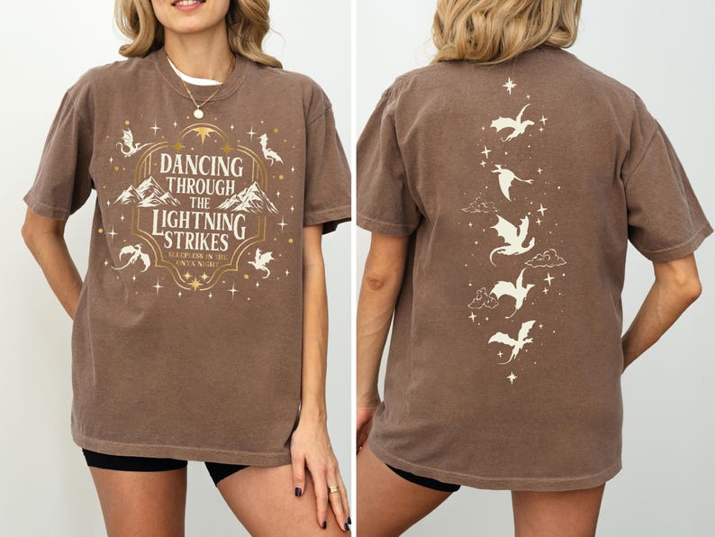 A woman wearing a brown t-shirt with a design featuring a dancing dragon and the text "Dancing through the lightning strikes".