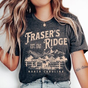A woman wearing a gray t-shirt with the text "Fraser's Ridge" and "North Carolina" printed on it, along with a mountain landscape graphic.