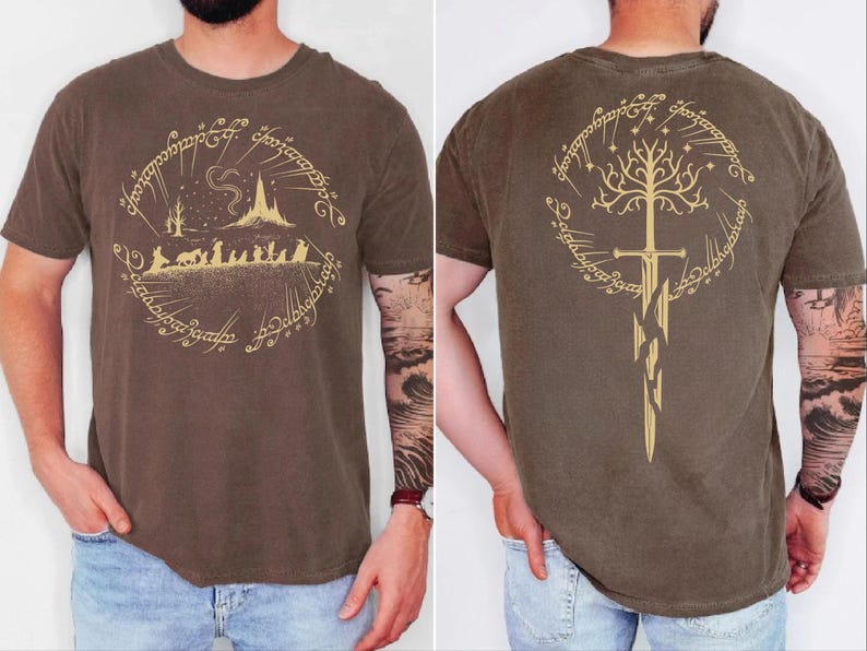 a man wearing a brown t-shirt with a graphic design featuring a castle, a tree, and a sword. The design is symmetrical, with the castle on the left and the sword on the right. The man has tattoos on his arms, and the back of the t-shirt displays the same design.