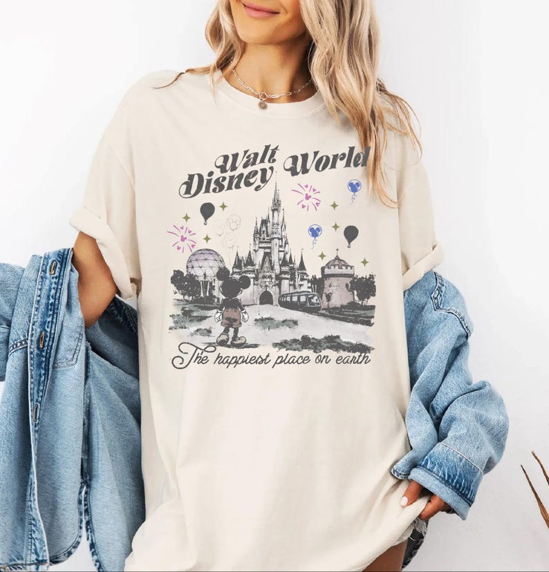 A woman wearing a white t-shirt with a graphic design of Disney World, including a castle, balloons, and the text "Disney World" and "The happiest place on earth".