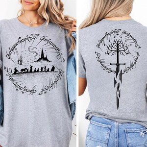 The image is a collage of two photos showing the back and front of a gray t-shirt with a graphic design featuring a castle, a tree, and a sword.