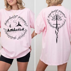 A woman wearing a pink t-shirt with a graphic design featuring a castle, a tree, and a sword.