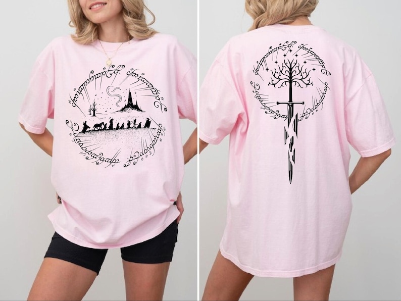 A woman wearing a pink t-shirt with a graphic design featuring a castle, a tree, and a sword.