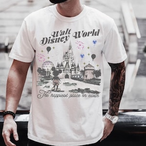 A man wearing a white t-shirt with a graphic design of a Disney castle and various Disney characters, including Mickey Mouse.