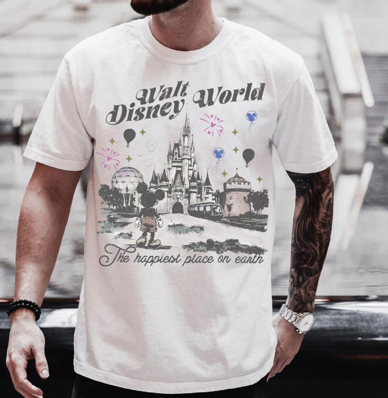 A man wearing a white t-shirt with a graphic design of a Disney castle and various Disney characters, including Mickey Mouse.