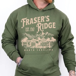 A man wearing a green hoodie with a graphic design of a mountain range and the text "Fraser's Ridge" printed on it.