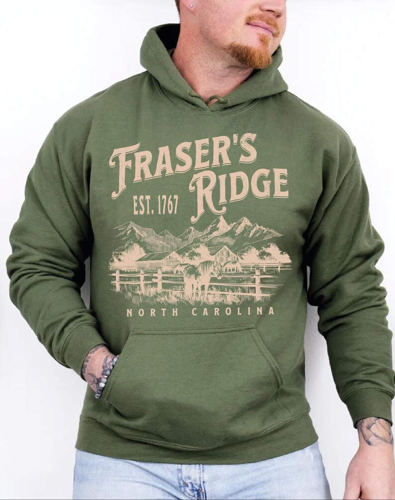 A man wearing a green hoodie with a graphic design of a mountain range and the text "Fraser's Ridge" printed on it.
