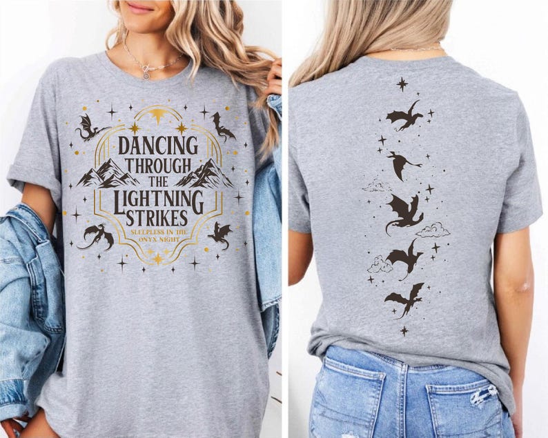 A woman wearing a gray t-shirt with a graphic design featuring a mountain range and the text "Dancing through the Lightning Strikes".