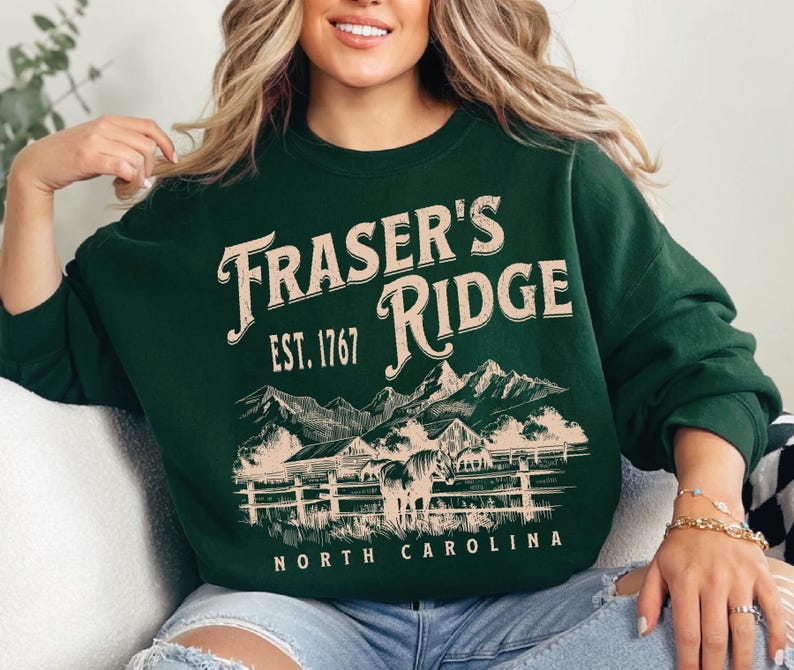A woman wearing a green sweatshirt with a graphic design of a mountain range and the text "Fraser's Ridge" printed on it.
