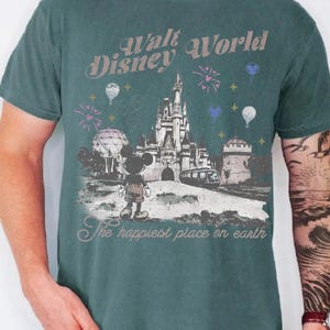 A man wearing a green t-shirt with a graphic design depicting Mickey Mouse and various Disney landmarks, including the Eiffel Tower and the castle.