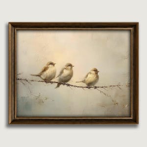 May include: A framed painting depicts three small birds perched on a thin branch. The birds have light brown and beige feathers. The background is a soft blend of beige and light blue hues, with a warm glow at the top. The frame is a dark brown color.
