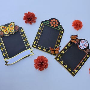 May include: Three black rectangular frames with yellow floral accents. The left frame features a yellow butterfly and a blank white banner. The center frame has a top flower and a monarch butterfly. The right frame includes a skull and butterfly.