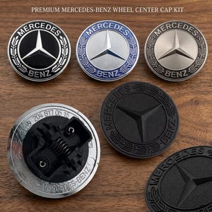 Può includere: Una collezione di kit di coprimozzi per ruote Mercedes-Benz. I coprimozzi presentano il logo Mercedes-Benz, una stella a tre punte, in vari colori tra cui nero, argento e blu. I testi "MERCEDES" e "BENZ" sono visibili.