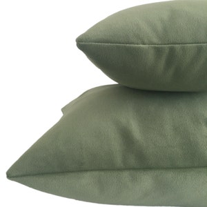 May include: Two sage green throw pillows stacked on top of each other. The pillows have a soft, textured appearance and a simple, minimalist design. The pillows are a solid color and have a seam running around the edges.