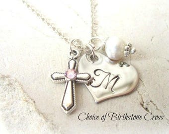 May include: Silver necklace with a heart charm engraved with the letter "M", a cross charm with a pink gemstone, and a pearl bead.
