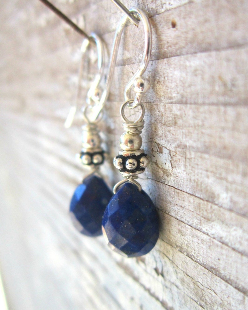 May include: A pair of silver earrings with blue gemstone drops. The earrings feature a silver bead with a textured surface and a silver hook.