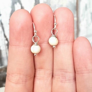May include: A pair of silver hoop earrings with small white bead dangles.