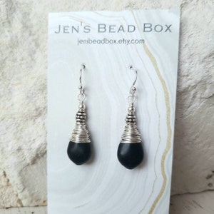 May include: Black gemstone earrings with silver wire wrapped around the stone and silver beads at the top of the wire. The earrings are hanging from silver hooks.