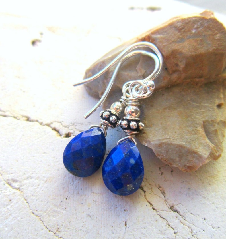 May include: A pair of silver dangle earrings with blue lapis lazuli gemstone drops. The earrings feature small silver beads and a wire wrapped design.