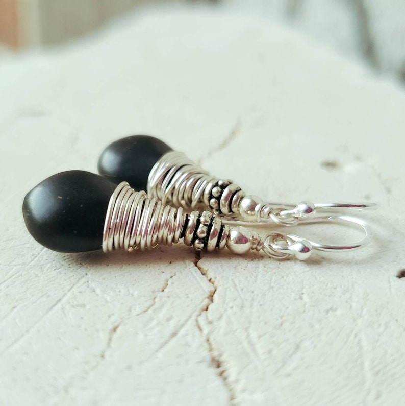 May include: A pair of silver earrings with black gemstone drops. The earrings are made with wire wrapped around the stones and have silver beads and hooks.