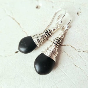 May include: A pair of dangle earrings with black gemstone drops wrapped in silver wire. The earrings have silver hooks.