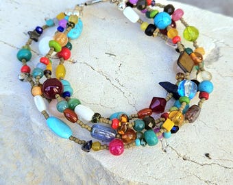May include: A multi-strand bracelet with a variety of colorful beads. The beads are in shades of blue, green, red, yellow, and purple. The bracelet is made of multiple strands of beads and has a silver clasp.