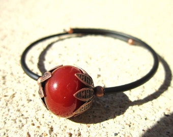 May include: A red carnelian gemstone bead with a copper leaf design is the focal point of this black elastic bracelet.
