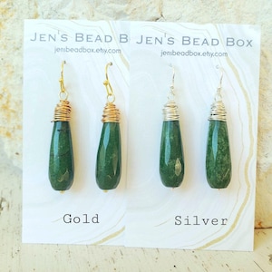 May include: Gold and silver wire-wrapped earrings with green teardrop-shaped stones. The earrings are displayed on a white card with the text "Jen's Bead Box" and the website address. The gold earrings have gold wire, and the silver earrings have silver wire.