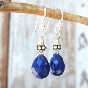 May include: A pair of silver dangle earrings with a teardrop-shaped lapis lazuli gemstone on each earring. The earrings have silver beads and a silver hook fastening.