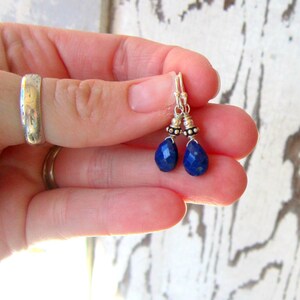 May include: A pair of silver dangle earrings with blue gemstone drops. The earrings feature small silver beads on the wire.