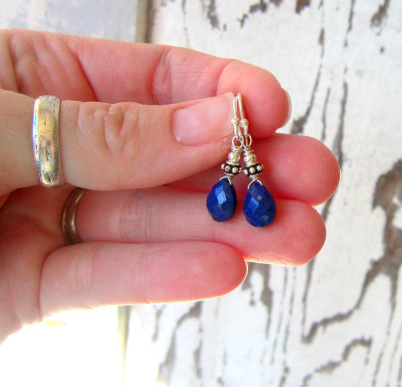 May include: A pair of silver dangle earrings with blue gemstone drops. The earrings feature small silver beads on the wire.