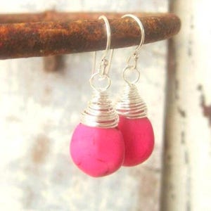 May include: A pair of drop earrings featuring vibrant hot pink, teardrop-shaped stones. Each stone is securely wrapped at the top with silver-toned wire, which transitions into a simple silver-toned hook for ear attachment and comfortable wear.
