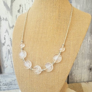 May include: A silver chain necklace with clear glass beads. The beads have a textured, frosted look.