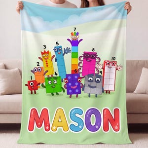 May include: A soft fleece blanket featuring the Numberblocks characters numbered one through ten in vibrant colors against a light green background. The name MASON is printed in large, colorful, bubble-style letters at the bottom of the blanket.
