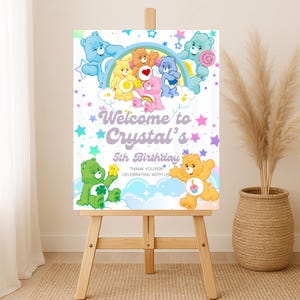 Puede incluir: Un caballete de madera exhibe un colorido letrero de cumpleaños. El letrero presenta osos de dibujos animados, un arcoíris y el texto "Welcome to Crystal's 5th Birthday". Estrellas y colores pastel decoran el letrero, con un mensaje de agradecimiento en la parte inferior.