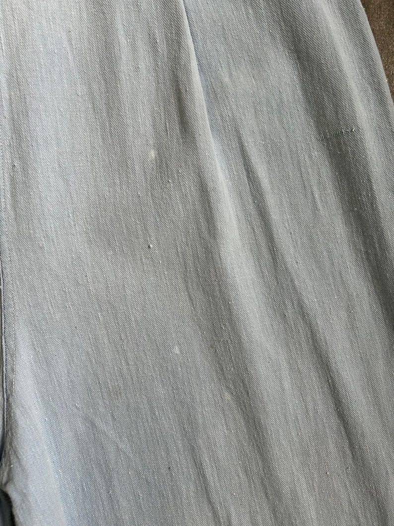 May include: Close-up of pale blue denim fabric. The fabric has a subtle texture and visible diagonal lines. There are a few small, light-coloured spots scattered across the surface. The overall appearance is soft and casual.