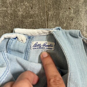 May include: Pale blue denim garment with a white collar. The label reads "Betty Brooks CALIFORNIA MADE". The fabric appears soft and worn. The garment is likely vintage.