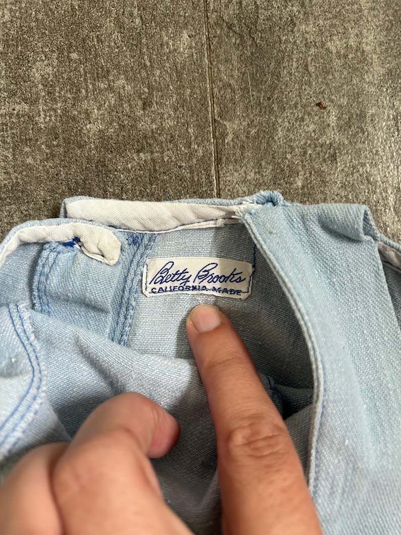 May include: Pale blue denim garment with a white collar. The label reads "Betty Brooks CALIFORNIA MADE". The fabric appears soft and worn. The garment is likely vintage.
