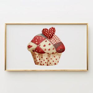 May include: A watercolour illustration of a cupcake with a patchwork design in red, white, and brown. The cupcake is topped with a red heart. The cupcake wrapper is beige with red polka dots. The image is in a gold frame.