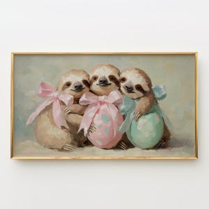 May include: A framed painting features three sloths with light brown fur, each holding a pastel-colored Easter egg. The sloths are adorned with pink and blue bows. The artwork has a soft, painterly style with a gold frame.