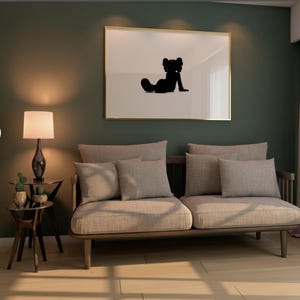 May include: A living room scene featuring a light-colored sofa with several matching pillows. A framed artwork with a black silhouette hangs above the sofa. A small side table with a lamp and decorative plants sits to the left.