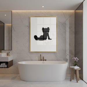 May include: A framed art print featuring a black silhouette of a seated figure with a distinctive head shape. The artwork is set against a white background within a gold frame. The print is displayed in a modern bathroom setting with a white bathtub.